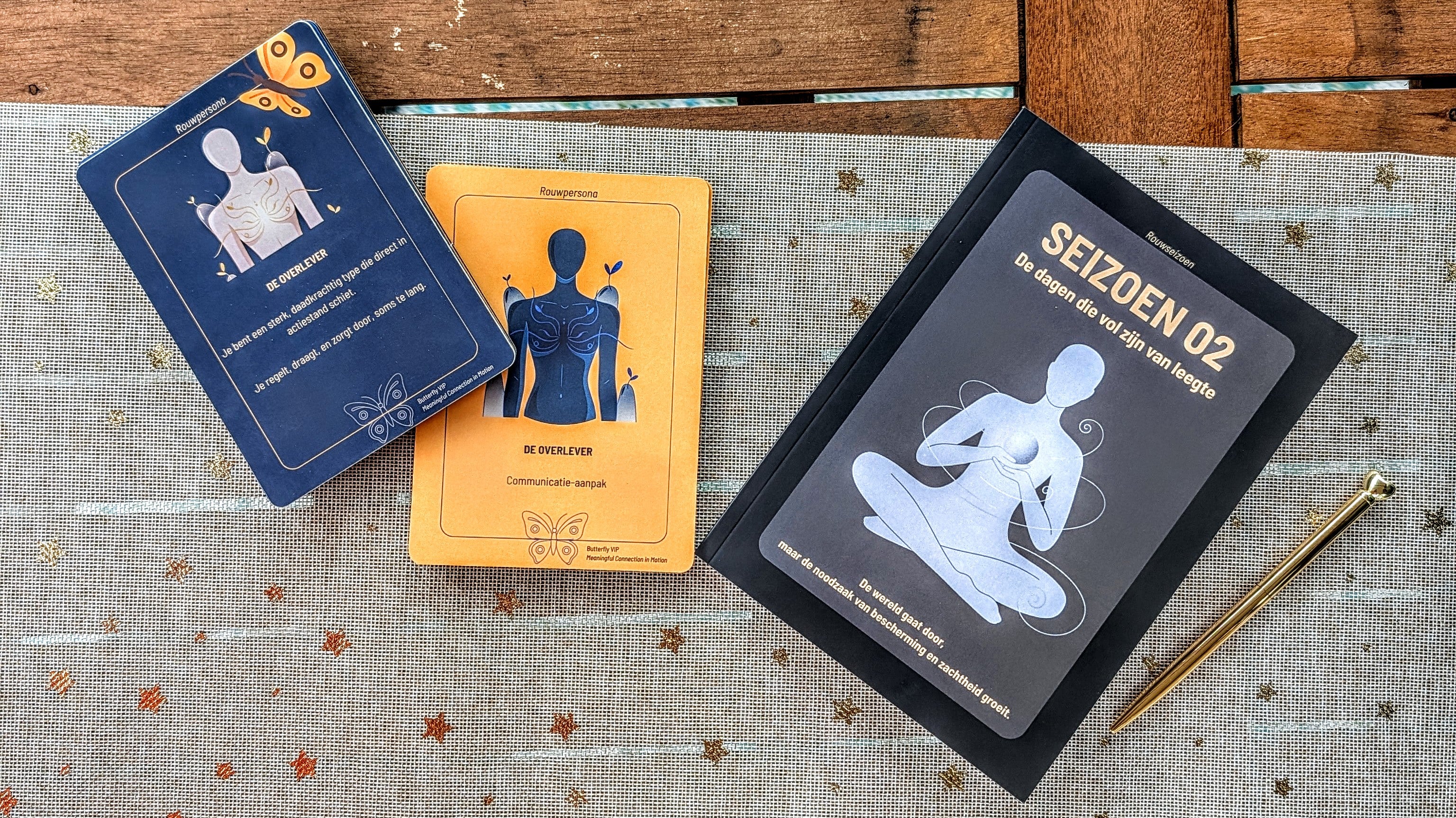 Kaartenset rouwpersona De Overlever links en rechts seizoen 02 reflectieboek met een pen ernaast om de schrijfopdrachten die erin staan aan te duiden.