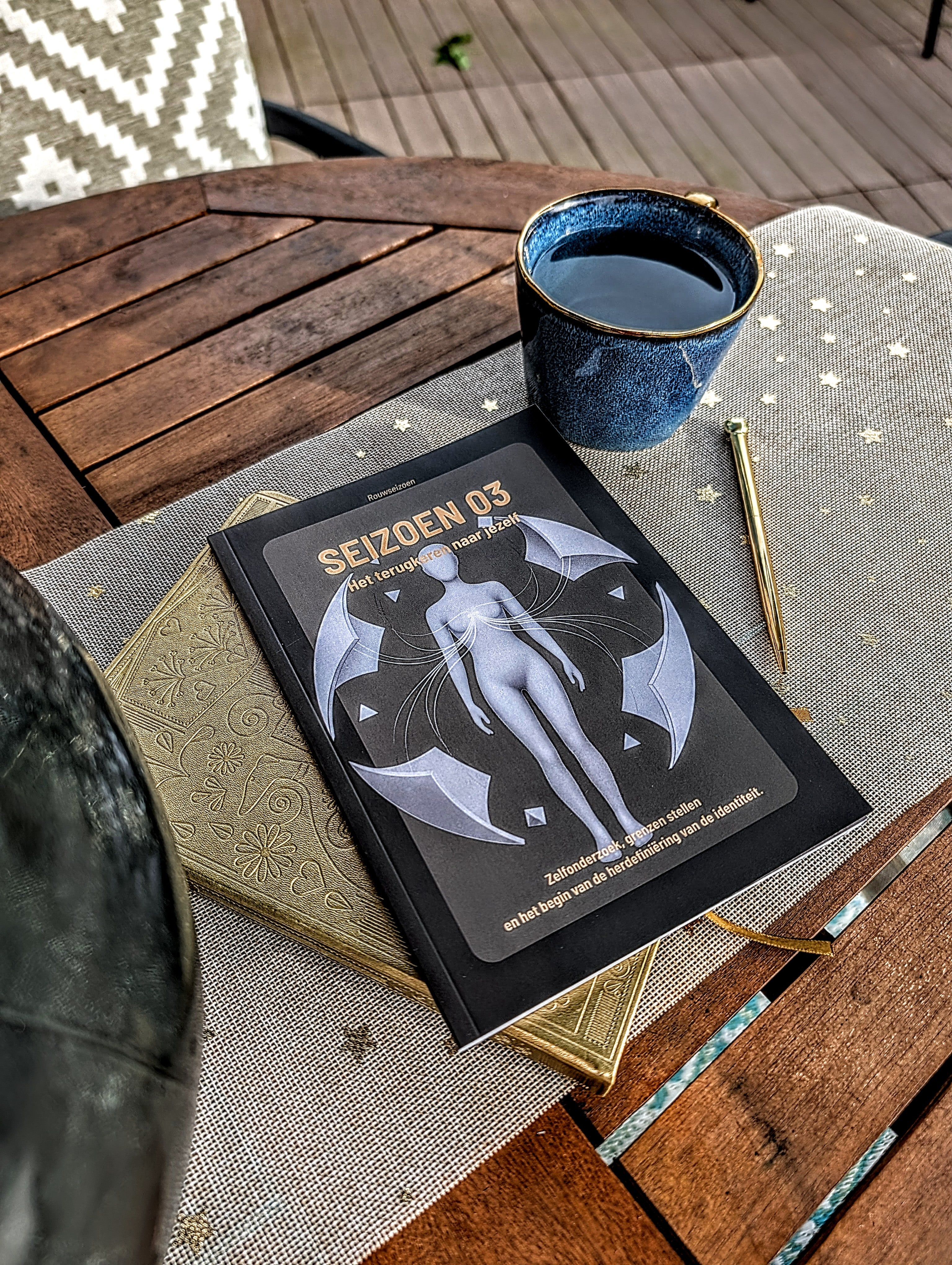 Seizoen 03 op tafel bovenop een notitieboek met een kop thee en pen ernaast.